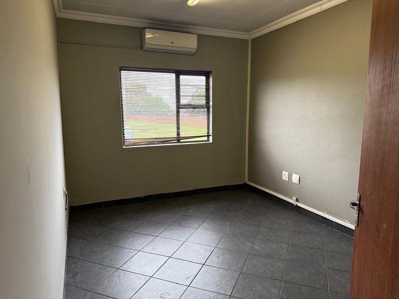 A vacant office space featuring dark tiled flooring, a wall-mounted air conditioning unit, and venetian blinds.