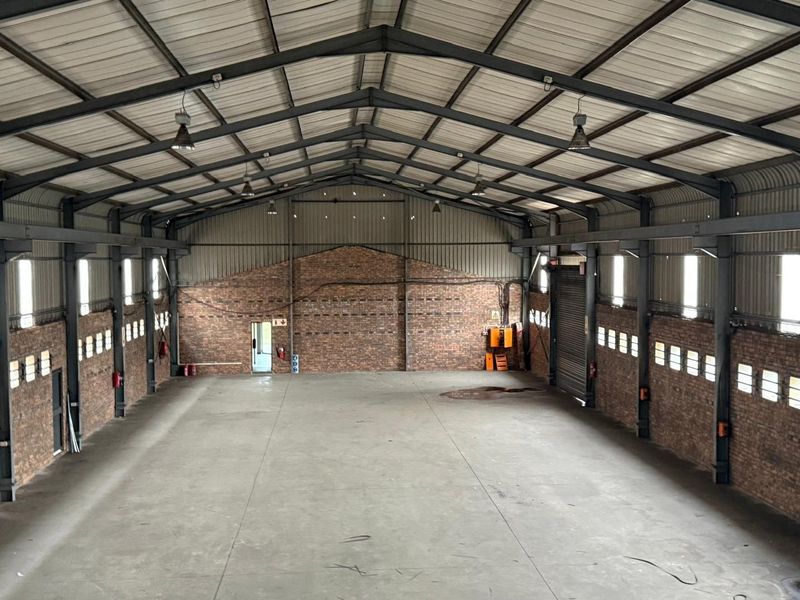 Spacious industrial warehouse featuring exposed brick walls, high-clearance steel portal frame, concrete flooring, and a large roller shutter door.