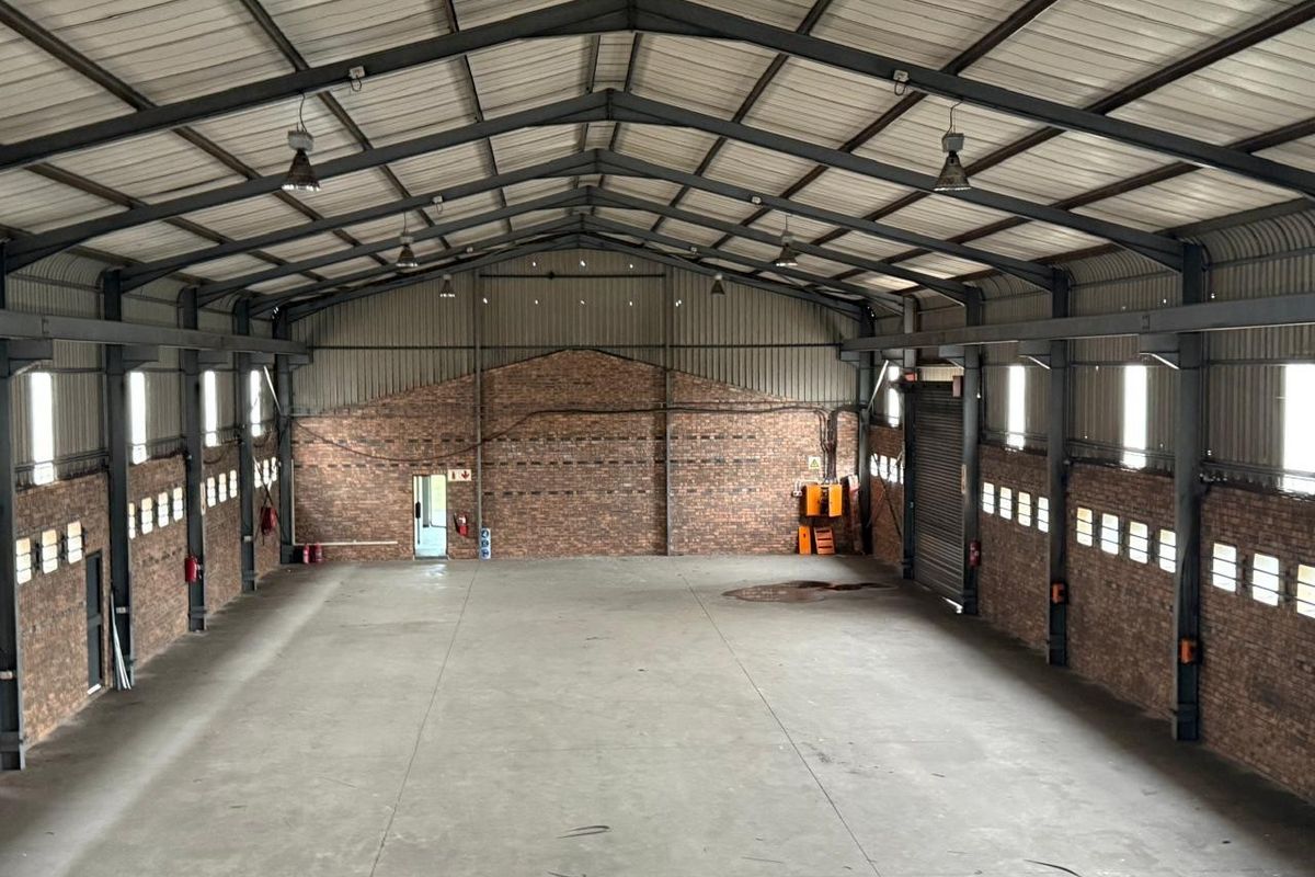 Spacious industrial warehouse featuring exposed brick walls, high-clearance steel portal frame, concrete flooring, and a large roller shutter door.