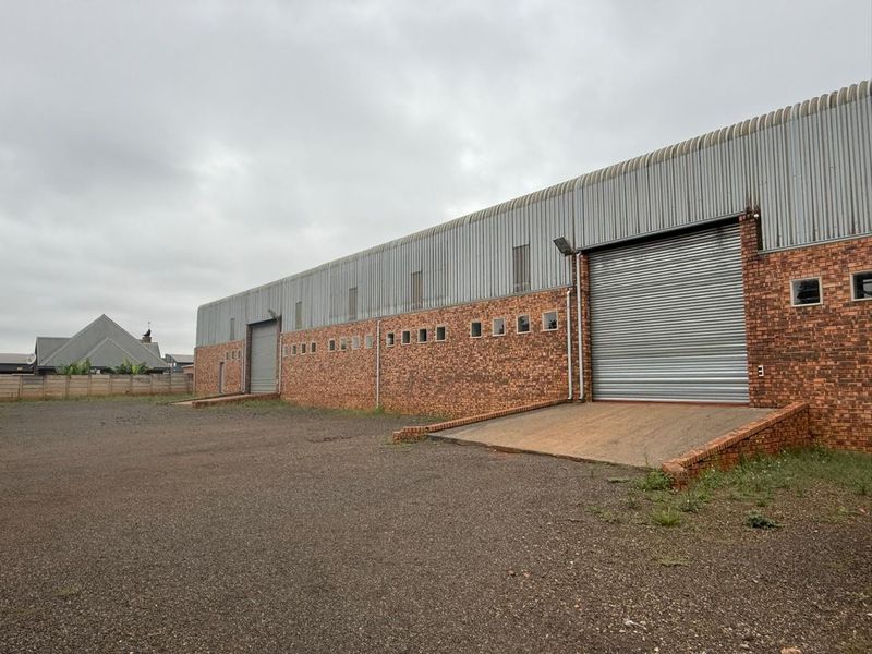 Industrial warehouse exterior featuring face brick construction, corrugated metal cladding, and multiple roller shutter doors with dedicated loading docks.