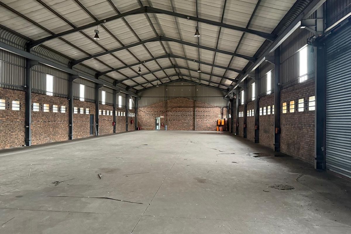 Spacious industrial warehouse featuring exposed brick walls, high-clearance steel portal frame, concrete flooring, and high-bay lighting, suitable for storage or manufacturing operations.