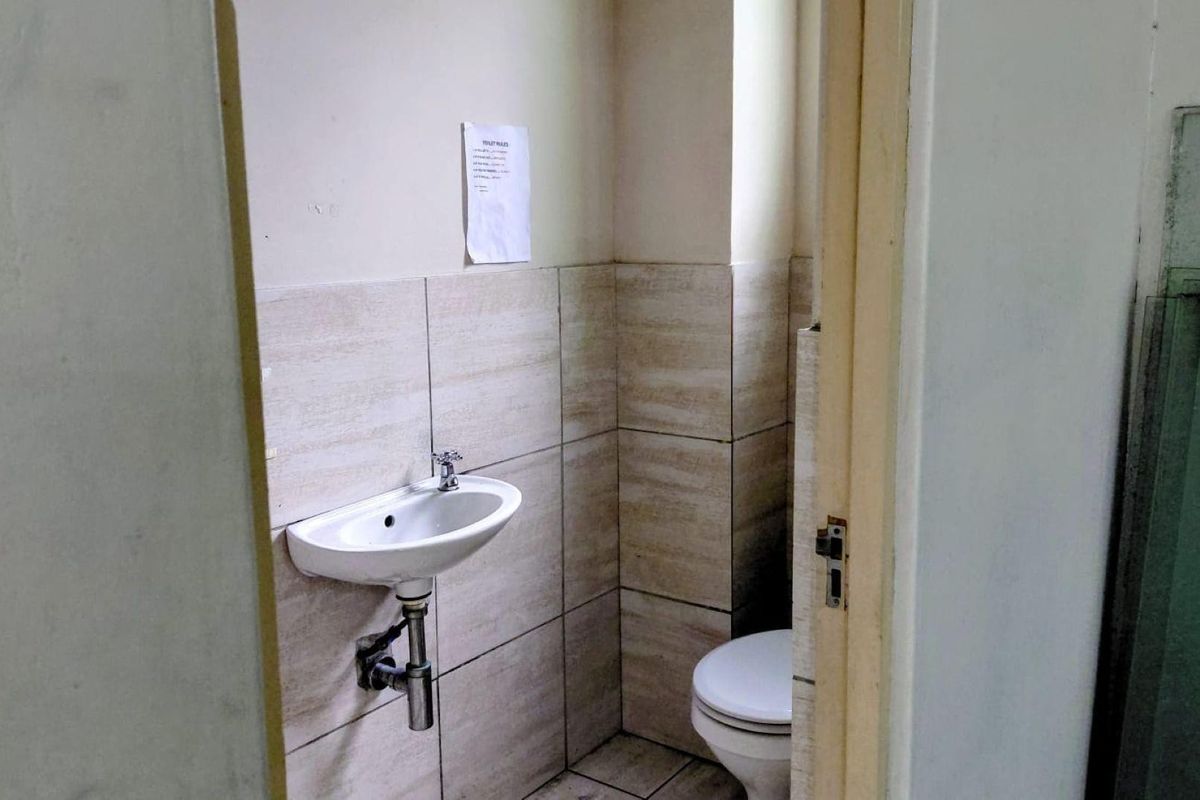 A compact industrial bathroom featuring a wall-mounted basin and toilet with neutral ceramic wall tiling.