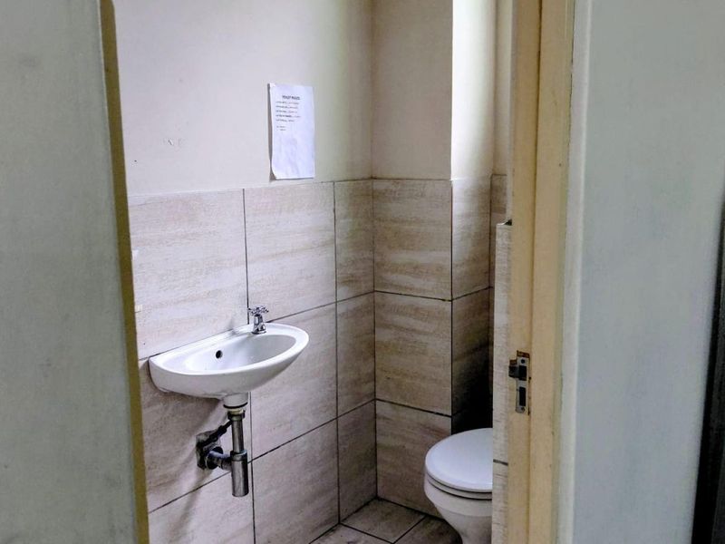 A compact industrial bathroom featuring a wall-mounted basin and toilet with neutral ceramic wall tiling.