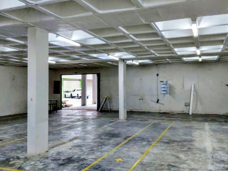 Spacious industrial utility area featuring a waffle slab ceiling, concrete flooring with painted markings, and functional overhead fluorescent lighting.