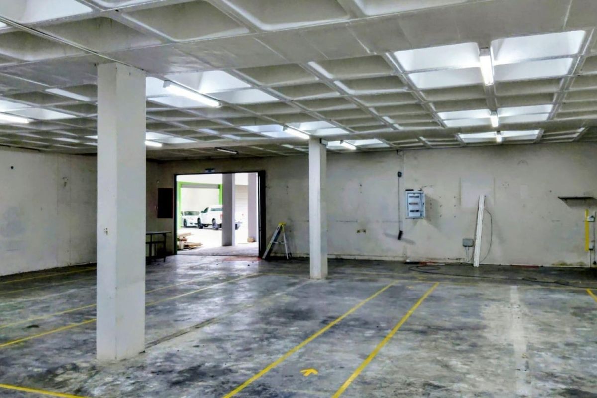 Spacious industrial utility area featuring a waffle slab ceiling, concrete flooring with painted markings, and functional overhead fluorescent lighting.