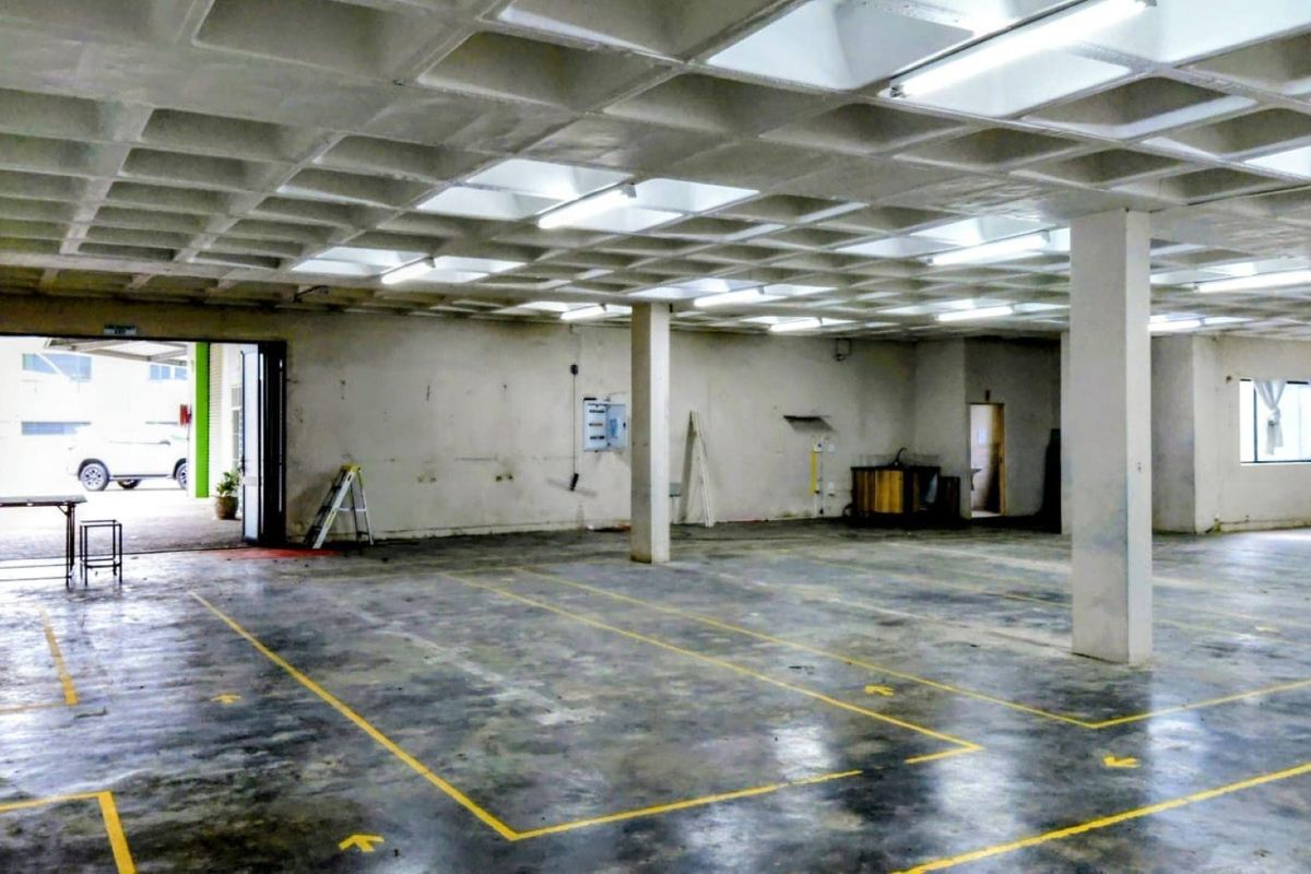 Spacious open-plan industrial unit featuring a waffle slab ceiling, concrete flooring with painted markings, and ample natural light from the entrance.