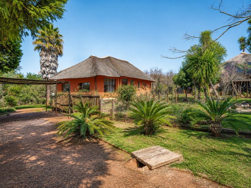 A view of a farm-style dwelling featuring a traditional thatch roof, surrounded by a landscaped garden and a covered carport area.