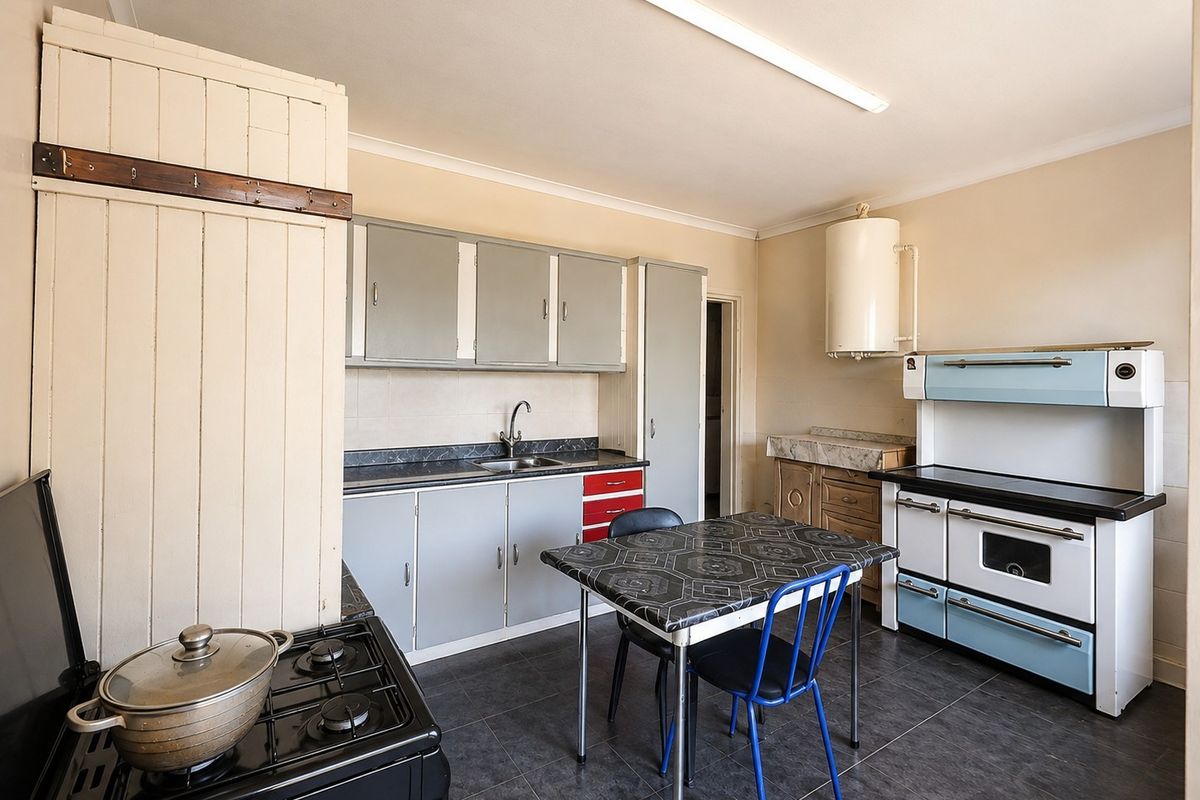 A functional farm-style kitchen featuring vintage cabinetry, a classic stove, and tiled flooring, offering potential for modernization and aesthetic updates.
