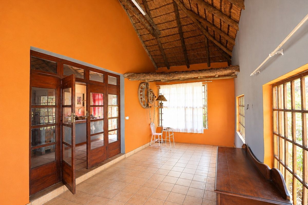 Spacious living area featuring a high vaulted thatched ceiling with exposed timber beams, tiled flooring, and large timber-framed glass doors leading to adjacent rooms.