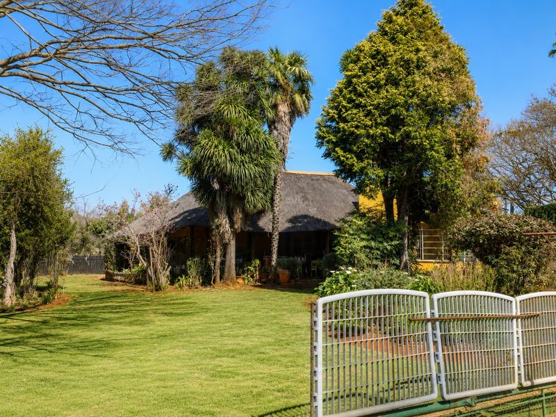 A view of the rear garden and property featuring a traditional thatch roof and a metal gate entrance.