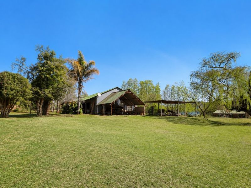 A wide view of the farm property featuring a main dwelling with a covered patio and an adjacent carport structure set on a large lawn.