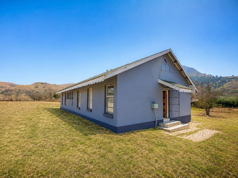 A side view of a rural farm building featuring a metal roof, security gate, and paved entrance steps set against a mountainous landscape.