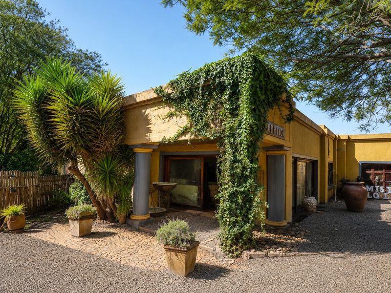 Front facade of the farm building featuring decorative columns, sliding glass doors, and a stone-paved entrance area surrounded by mature landscaping.