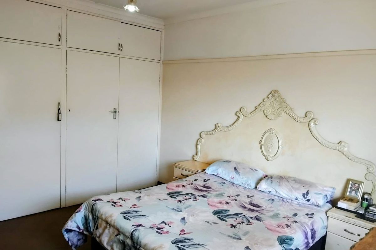 A bedroom featuring built-in cupboards and a decorative headboard, requiring cosmetic updates to the wall finishes and paintwork to modernize the space.