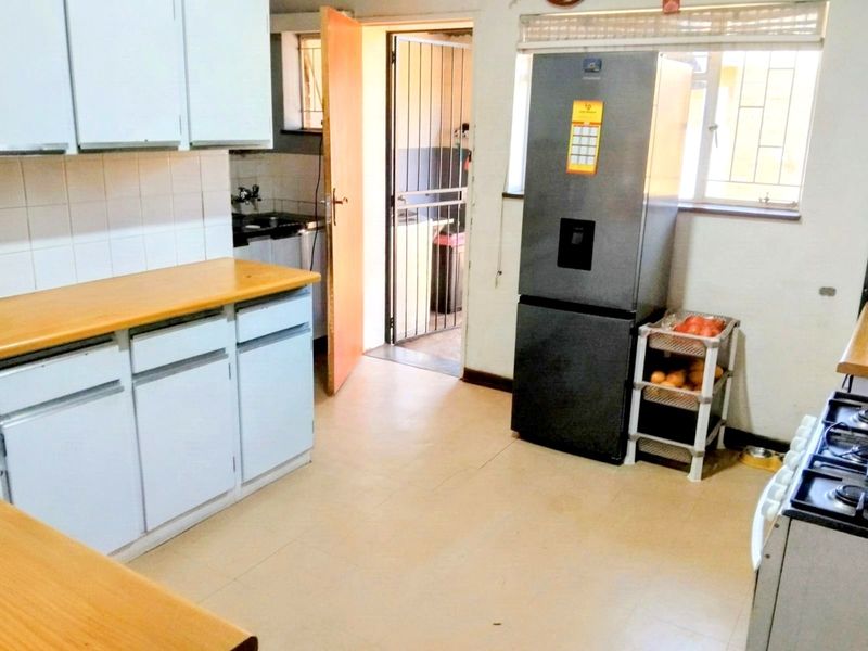 A functional kitchen featuring laminate countertops, built-in cabinetry, and a tiled backsplash, with direct access to an exterior area via a security gate.
