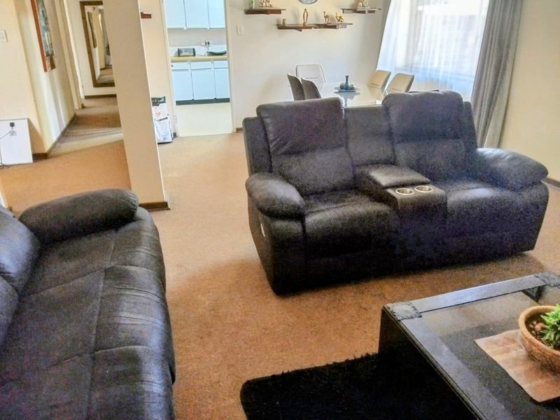 Open plan living and dining area with carpeted flooring, leading through an archway to a secondary kitchen or scullery space.