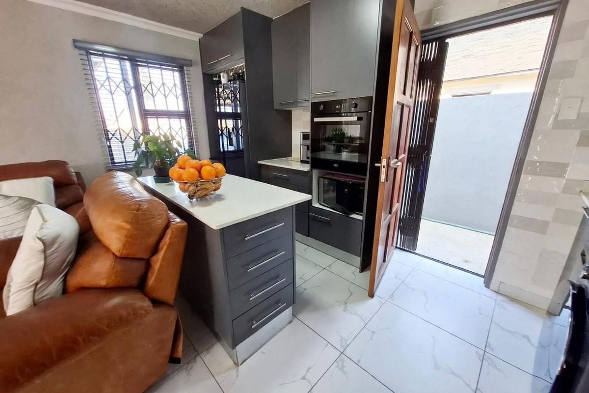 Modern kitchen featuring dark cabinetry, stone countertops, built-in oven, and tiled flooring with direct access to an outdoor area.