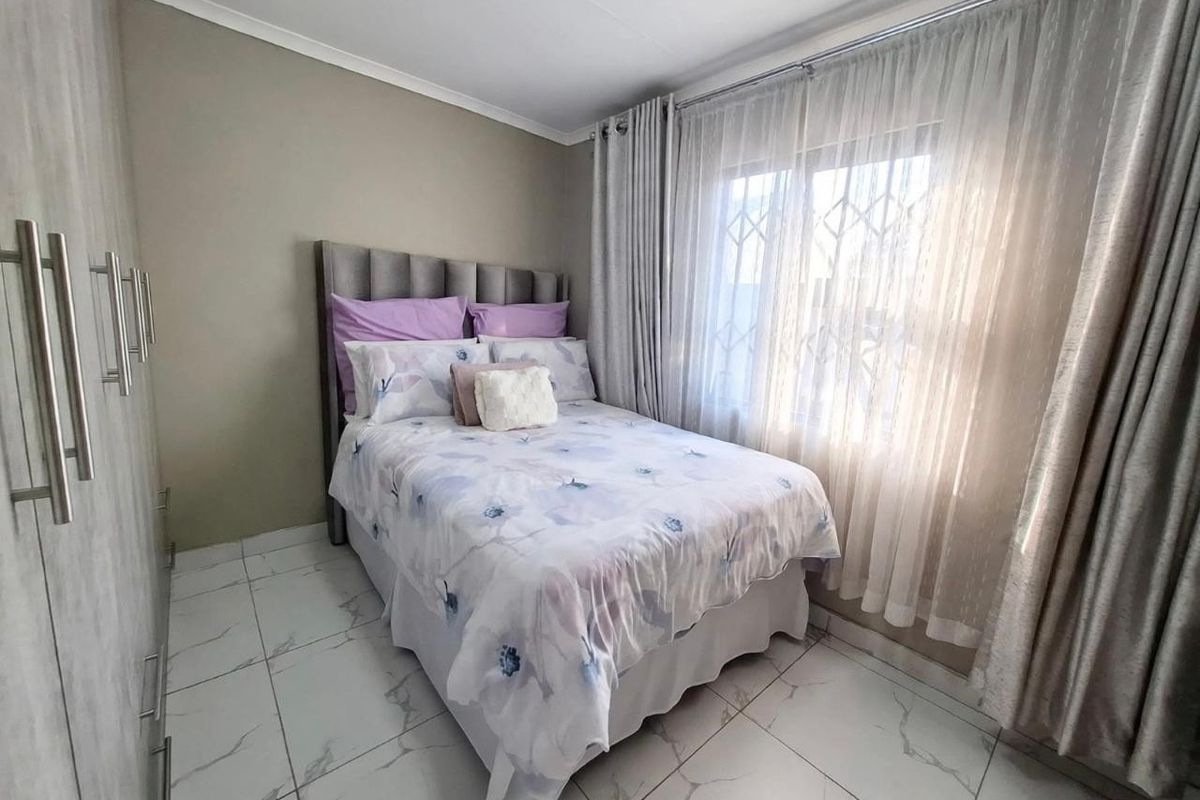 A well-maintained bedroom featuring modern tiled flooring, built-in cupboards, and a window fitted with security bars and curtain rails.