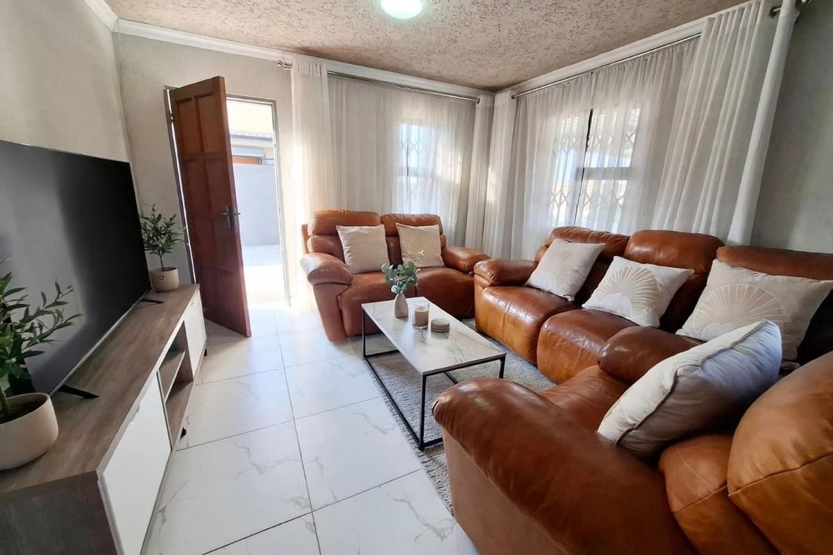 A comfortable living room featuring light-colored tiled flooring, a textured ceiling, and natural light entering through windows fitted with security bars.