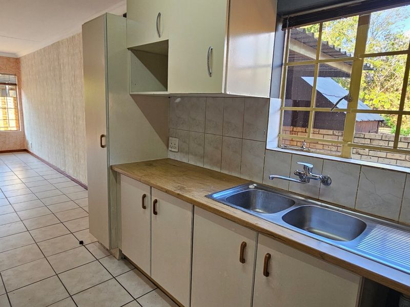 A functional kitchen area featuring built-in cabinetry, laminate countertops, and a double bowl stainless steel sink, with tiled flooring throughout.