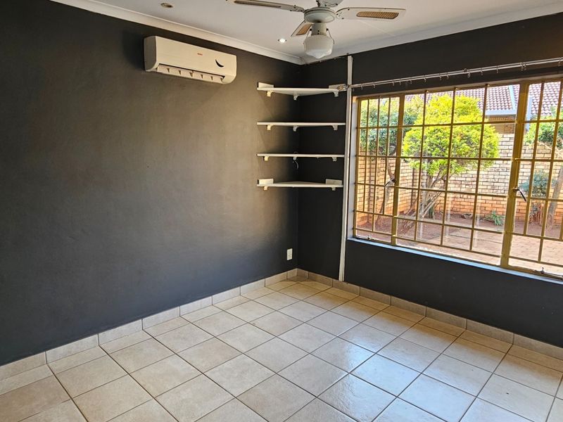 An empty bedroom featuring dark painted walls, tiled flooring, a ceiling fan, a wall-mounted air conditioning unit, and built-in shelving.
