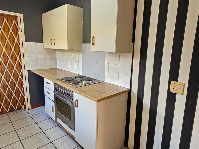 A compact kitchen featuring built-in cabinetry, a laminate countertop, an integrated electric hob and oven, and tiled flooring with a security gate entrance.