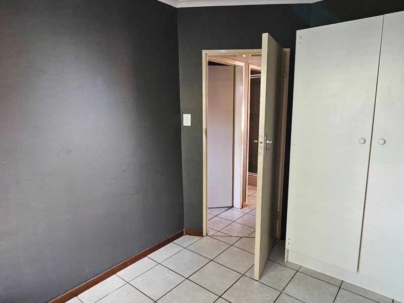 A bedroom featuring dark painted walls, tiled flooring, and a built-in wardrobe, offering a blank canvas for personalization.