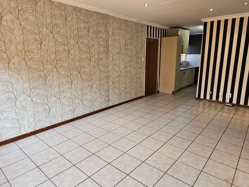 An open-plan living and kitchen area featuring tiled flooring, recessed lighting, and distinct patterned wallpaper, offering a blank canvas for renovation.
