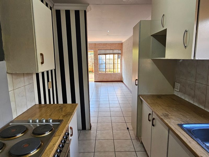 A functional kitchen featuring built-in cabinetry, laminate countertops, an electric hob, and an integrated oven, leading into an open-plan living area with tiled floors.