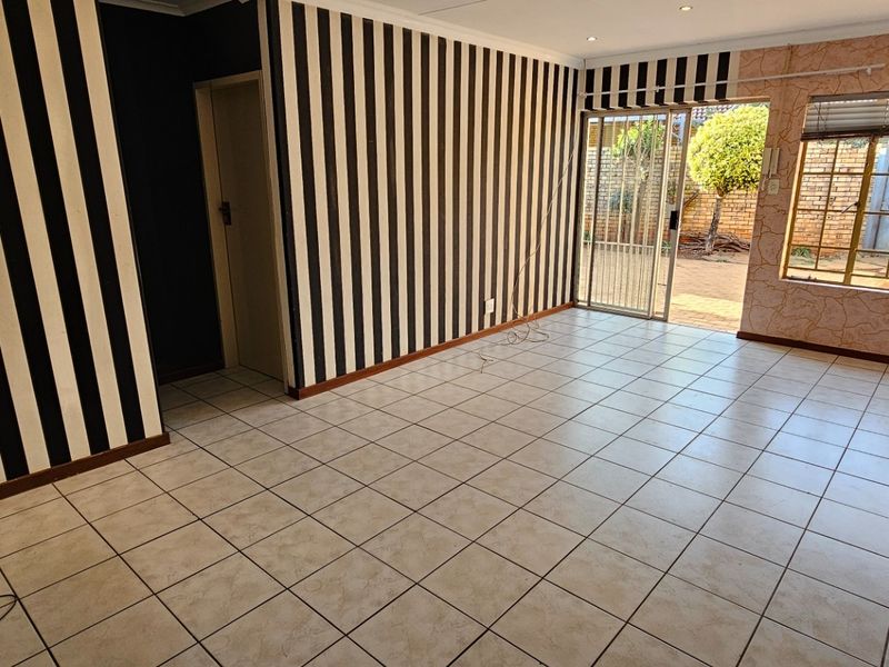 An empty living room featuring tiled flooring, recessed lighting, and access to an outdoor area through a sliding glass door with security gate.