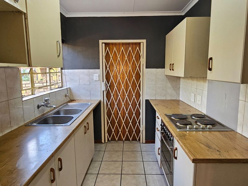 A functional kitchen featuring built-in cabinetry, laminate countertops, a double sink, and integrated electric cooking appliances with tiled flooring and backsplash.