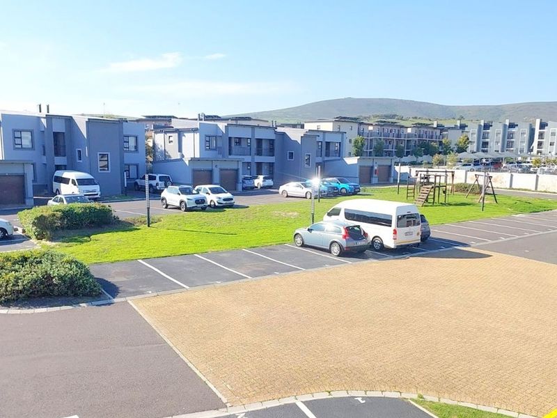An elevated view of the apartment complex grounds, featuring paved parking bays, communal green spaces, and a small playground area.