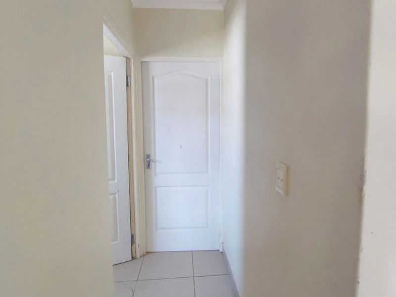 A simple, neutral-toned hallway featuring tiled flooring and access to internal rooms.