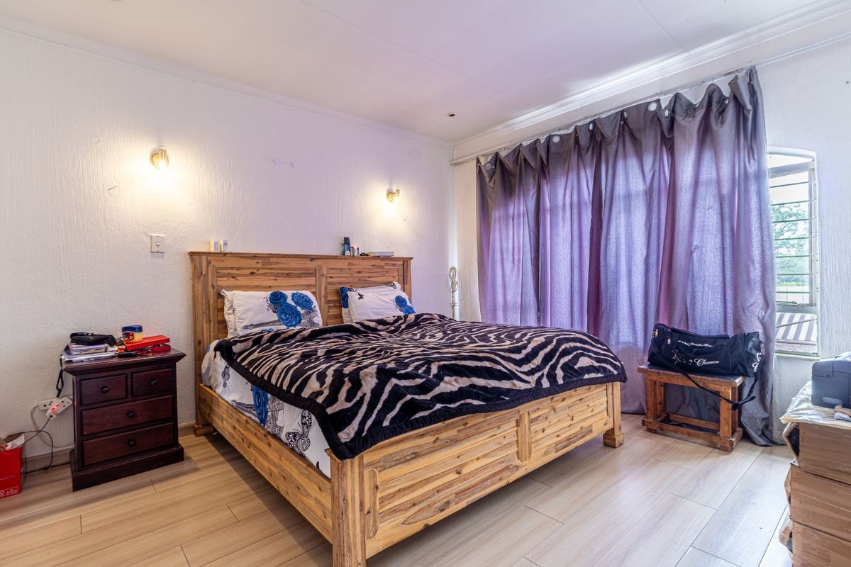 A bedroom featuring light-toned laminate flooring, wall-mounted lighting, and large windows with curtain tracks, providing a functional space with neutral finishes.