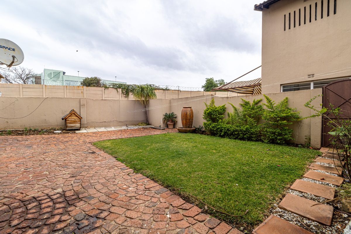 A private rear courtyard featuring a combination of brick paving and a small lawn, enclosed by a perimeter wall with a retractable awning.