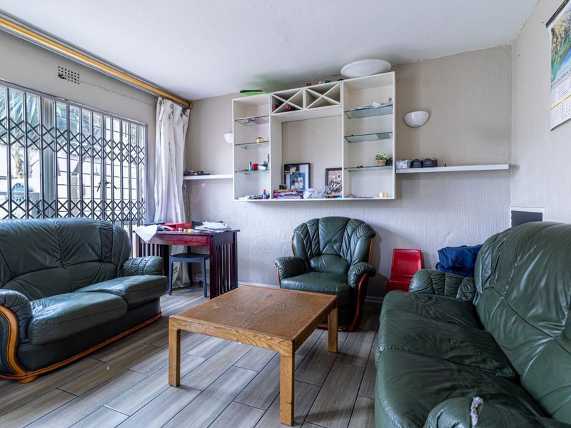 A living room featuring tiled flooring, a built-in wall shelving unit, and a security gate over the window, offering a functional layout for renovation.