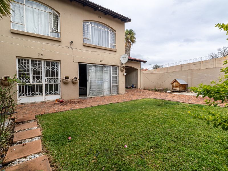 Rear exterior view of the townhouse featuring a brick-paved patio, a small lawn, and secure perimeter walling with razor wire.