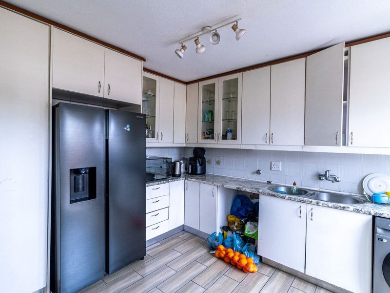 A functional kitchen featuring laminate cabinetry, granite countertops, a double bowl sink, and tiled flooring, offering a practical layout with ample storage space.