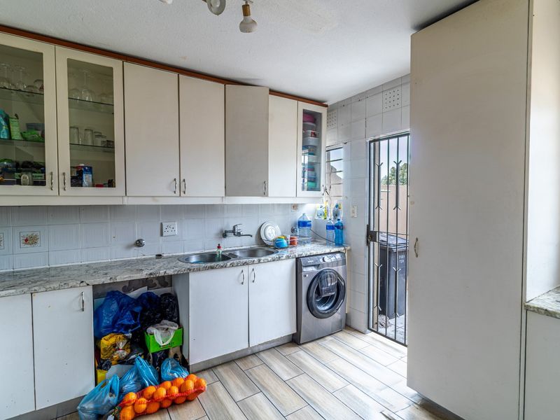 A functional kitchen featuring built-in cabinetry, a double basin sink, and tiled finishes, with direct access to an exterior area via a security gate.