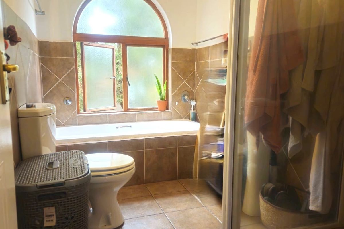 A functional bathroom featuring a built-in bathtub, a separate shower enclosure, and tiled finishes with an arched window providing natural light.
