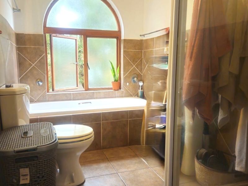 A functional bathroom featuring a built-in bathtub, a separate shower enclosure, and tiled finishes with an arched window providing natural light.