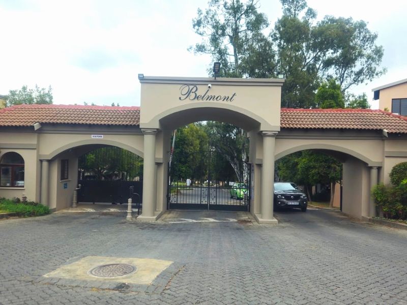 The main entrance gate to the Belmont residential complex, featuring a secure access point, paved driveway, and established landscaping.