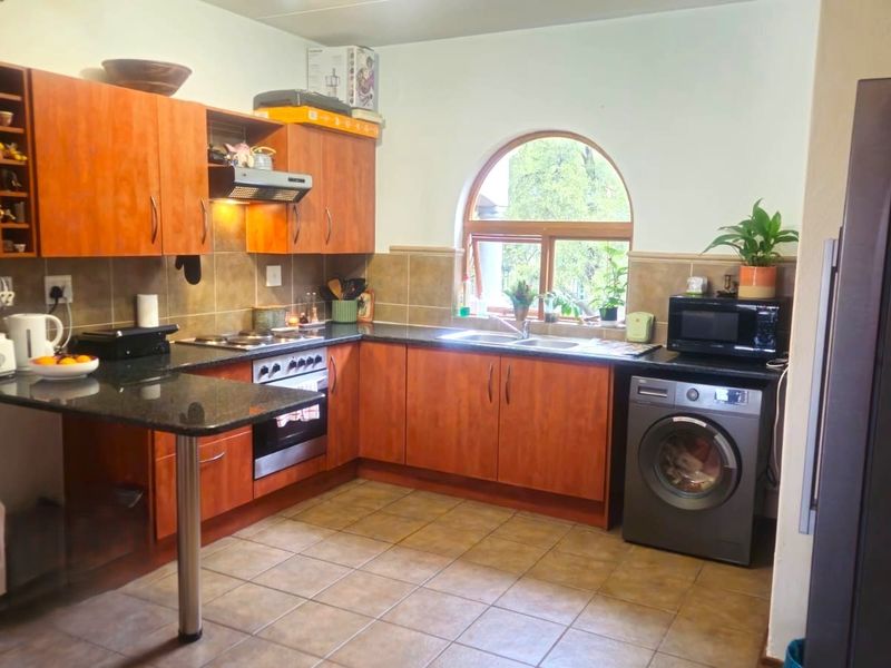 A functional kitchen featuring warm-toned wooden cabinetry, granite countertops, a built-in oven with hob, and a distinctive arched window providing natural light.