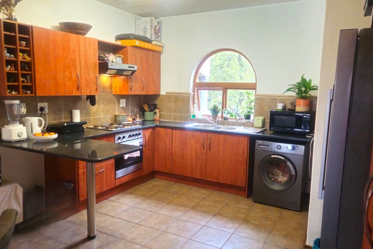 A functional kitchen featuring warm-toned wooden cabinetry, granite countertops, a built-in oven with hob, and a distinctive arched window providing natural light.