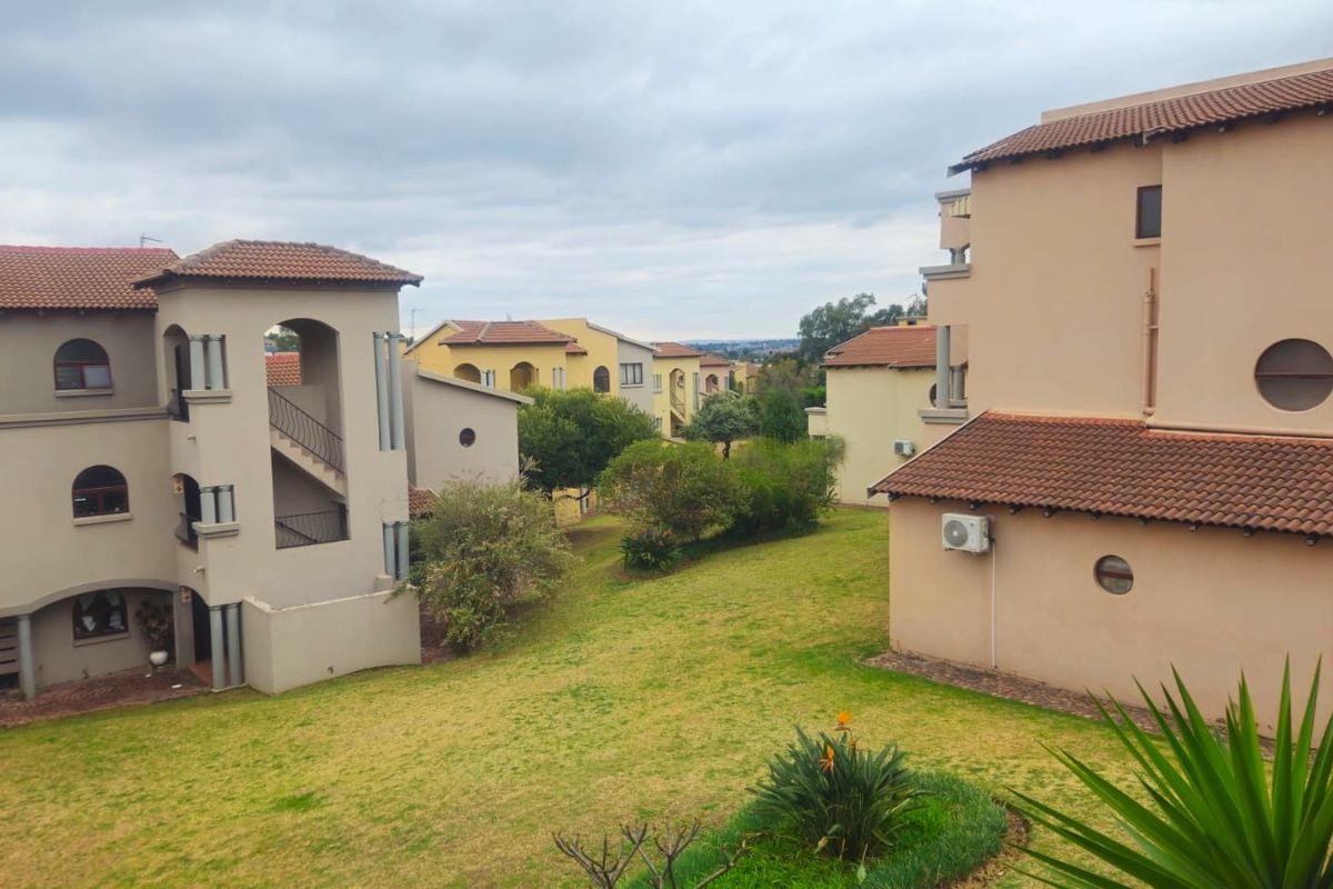 View of the apartment complex rear exterior, featuring landscaped garden areas, terracotta roof tiles, and multi-level building facades.