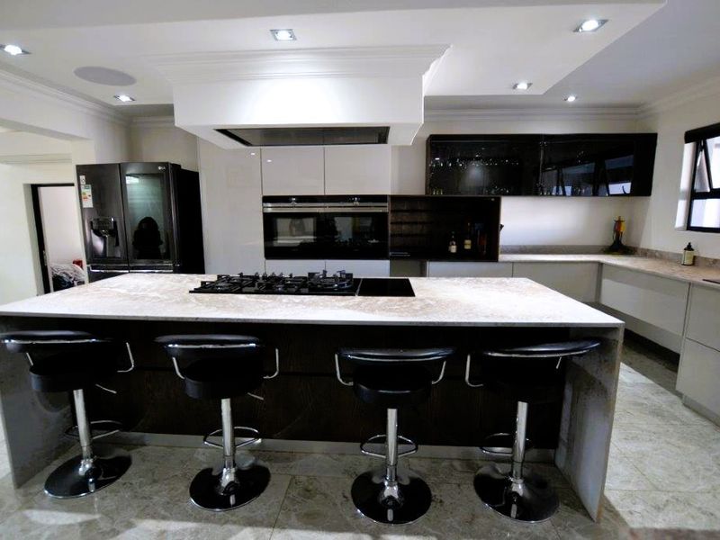 Modern kitchen featuring a large central island with a gas hob, stone countertops, built-in ovens, and sleek cabinetry with recessed lighting.