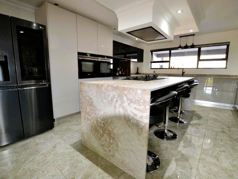 Modern kitchen featuring a large stone-topped island, built-in appliances, sleek cabinetry, and high-quality tiled flooring.