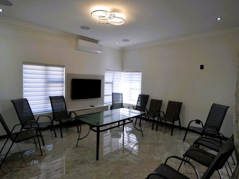 A spacious living area featuring polished tiled flooring, recessed ceiling lighting, a wall-mounted air conditioning unit, and modern zebra blinds.
