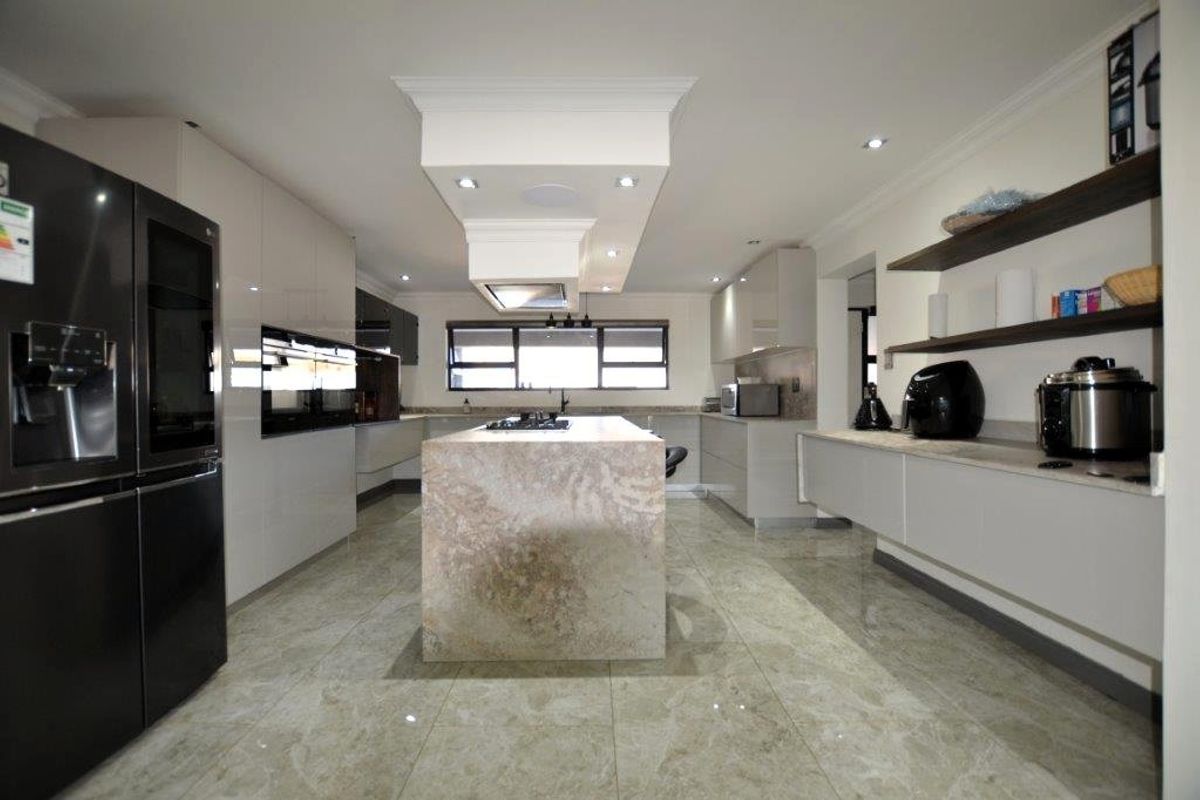 Modern kitchen featuring a central stone-topped island, high-gloss cabinetry, built-in appliances, and polished tiled flooring with recessed ceiling lighting.