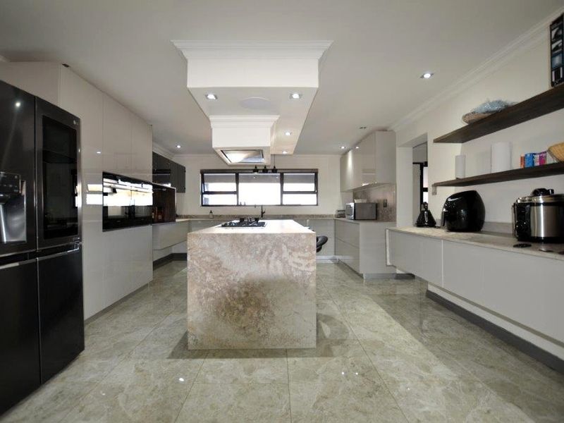 Modern kitchen featuring a central stone-topped island, high-gloss cabinetry, built-in appliances, and polished tiled flooring with recessed ceiling lighting.